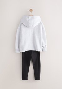 Grauer Kapuzenpullover mit lockerem Sitz und gerippten Bündchen, kombiniert mit schwarzen Stretch-Leggings, vor einem neutralen Hintergrund hängend.