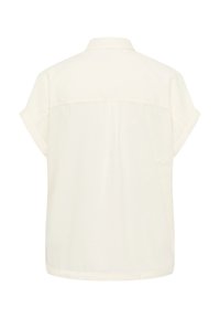 Short-sleeved, cream-colored blouse made of lightweight fabric with a back yoke and a classic collar, featuring rolled sleeves.