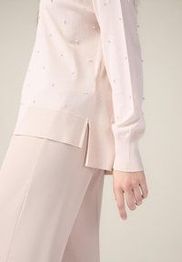 Suéter rosa claro con adornos de perlas, dobladillo acanalado y aberturas laterales. Combinado con pantalones suaves rosa a juego, de textura lisa.