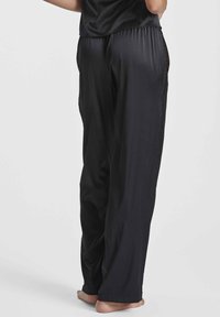 Pantalons de sport noirs avec une texture lisse et brillante et des panneaux latéraux en maille. Coupe ample avec une taille élastique, se resserrant aux chevilles.