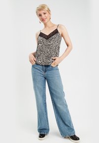 Schwarzes und beiges Leopardenmuster-Camisole mit Spitzenbesatz, kombiniert mit hellblauen weit geschnittenen Jeans und schwarzen Plateaustiefeln.