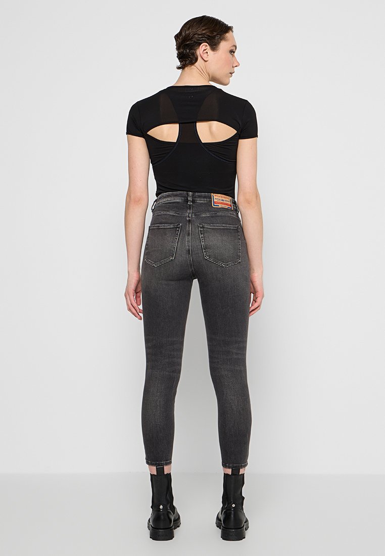 Schwarzes ergonomisches Oberteil mit einem Ausschnitt im Rückenbereich, kombiniert mit hoch taillierten, ausgebleichten grauen Skinny-Jeans und schwarzen Ankle Boots.