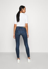 Tynne denim jeans med en mørkeblå vask, fem lommer og sydd detaljer. Sammen med en hvit kortermet topp og hvite sneakers.