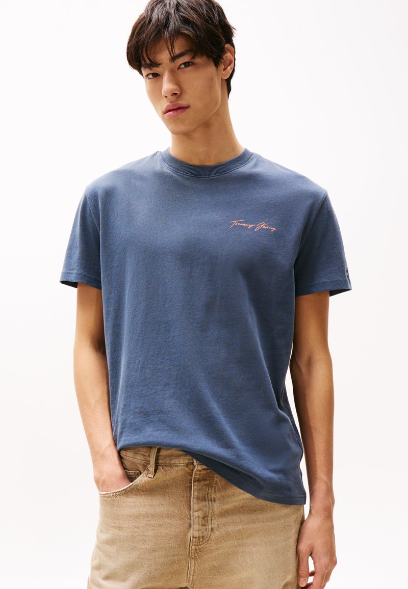 Navy bomull t-skjorte med rund hals og korte ermer. Har liten rosa "Tommy Jeans" logo ved brystet. Løs passform.