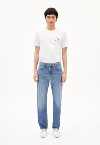 Witte katoenen t-shirt met een ronde halslijn en een kleine grafische afbeelding op de linkerkant van de borst, gecombineerd met lichtblauwe rechte spijkerbroek.