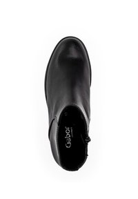Bottine en cuir noir avec une texture lisse, bout rond, fermeture éclair sur le côté et un talon bas et robuste. Marque intérieure visible en blanc.