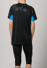 Camiseta deportiva negra con mangas azules, con un diseño texturizado en la parte posterior, combinada con leggins de compresión negros.