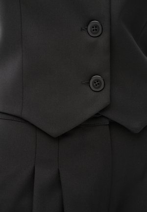 Czarna dopasowana kamizelka garniturowa z dwoma czarnymi guzikami, zestawiona z czarnymi spodniami o podobnym odcieniu, ukazująca fakturę tkaniny i szczegóły szwów.
