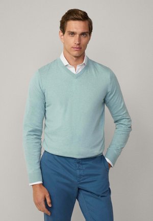 Pull bleu clair en V fait d'un matériau doux, associé à un pantalon bleu foncé. Le pull a des manches longues et un design ajusté.
