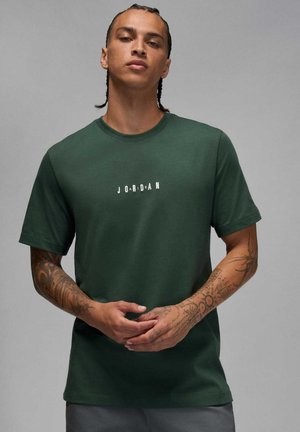 T-shirt verde a maniche corte in cotone, con un logo centrale bianco "JORDAN" in stili di lettere misti. Texture liscia e vestibilità regolare.