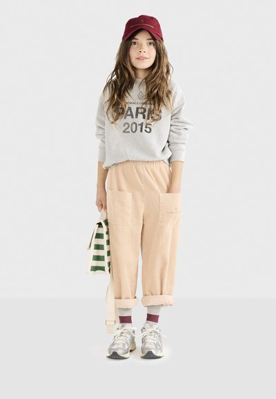 Sudadera gris con el texto "PARIS 2015", pantalones de pana beige con grandes bolsillos, gorra burdeos, zapatillas gris y blancas, bolso verde rayado.