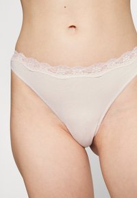 Lichtroze stringondergoed met een bloemenkant tailleband, gemaakt van zachte katoen met een gladde textuur en nette stiksels.
