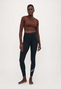 Brun langermet crop top med blomstermønster, sammen med svarte leggings med hvit logo på siden. Glatt stoff, tettsittende design.