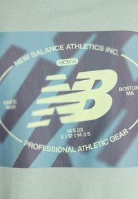 Light blue athletic t-shirt featuring a graphic print in blue and gray. Includes "New Balance Athletics Inc." and logo. Smooth fabric texture.