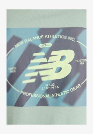 Ljusblå atletisk t-shirt med grafiskt tryck i blått och grått. Innehåller "New Balance Athletics Inc." och logotyp. Slät tygtextur.