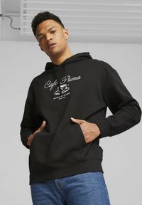 Black hoodie with front pocket, featuring white text "Cafe Puma" and a coffee cup graphic. Soft fabric with ribbed cuffs and hem.