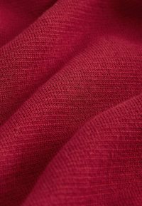 Textílie v tmavo červenej farbe so jemným, štruktúrovaným povrchom. Tkanina zobrazuje jemný pletený vzor s miernou variáciou v textúre pozdĺž záhybov.