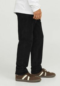 Svarta kordflöjtsbyxor med rak passform, med vertikal ribbstruktur och sidofickor. Bärs tillsammans med bruna sneakers med vita detaljer.