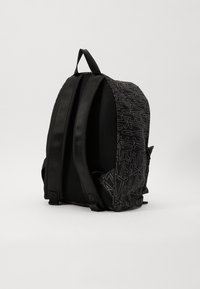 Zaino nero con tessuto testurizzato, caratterizzato da un motivo geometrico grigio scuro, spallacci imbottiti e una maniglia superiore per il trasporto.