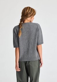 Rövid ujjú, szürke kötött pulóver bordázott aljjal és nyakkal; puha tapintású, laza szabású, látható minták vagy fémrészek nélkül.