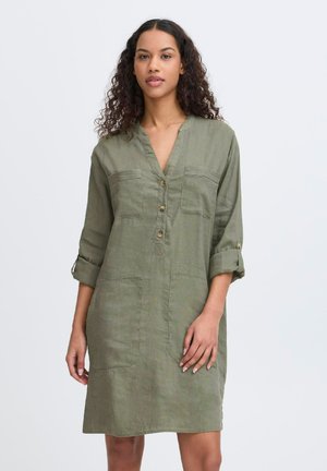 Robe en lin vert olive avec un décolleté en V, boutons à l'avant, deux poches poitrine et manches retroussées. Texture lisse, design arrivant au genou.