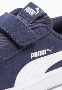 Zapatillas azul marino con correas de velcro, material de ante y un logo de Puma en blanco. Presentan un tejido texturizado y una suela blanca en contraste.