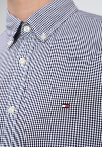 Košile s knoflíky v kostkovaném vzoru námořnické modře a bílé barvy, vybavená strukturovaným límcem, bílými knoflíky a malým značkovým logem na hrudi.
