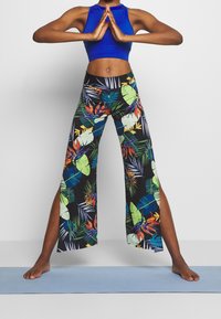 Blå kort topp med svarta, blommönstrade vida byxor som har gröna blad och livfulla blommor, designade för komfort och rörelse.