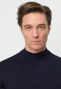 Marinefarbener Pullover mit hohem Kragen aus weichem Stoff, verfügt über gerippte Details am Kragen, schlanke Passform und glatte Textur.