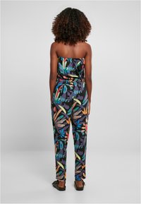 Mono con estampado floral en tela negra, con un diseño sin tirantes, cintura elástica y pantalones holgados, combinado con sandalias planas negras.