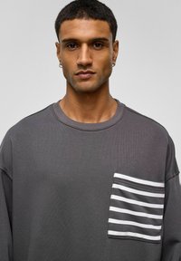 Grijze sweatshirt met een ronde hals, voorzien van een borstzak aan de linkerkant versierd met witte horizontale strepen. Zacht, gestructureerd materiaal.