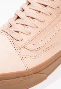 Gros plan d'une basket beige avec des lacets en tissu, une tige en cuir cousu, et une semelle en caoutchouc texturée de couleur marron clair.