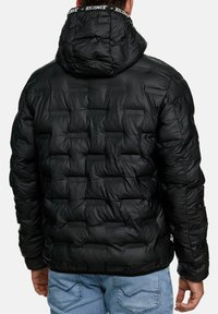 Giacca puffo nera con design trapuntato, dotata di cappuccio e bordino del collo con logo. Il materiale appare lucido e strutturato.
