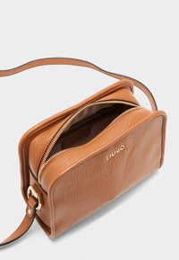 Bruin leren crossbody tas met een gestructureerde afwerking, gouden hardware en een ritssluiting. Binnenzijde toont het merkteken en is bekleed met stof.