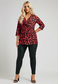 Top a righe rosse e nere con nodo in vita, abbinato a pantaloni neri aderenti e tacchi neri con cinturini. Il tessuto principale è liscio.