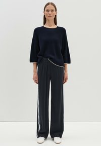Marineblauer, gerippter Strickpullover mit rundem Halsausschnitt und Dreiviertelärmeln, kombiniert mit schwarzen, weiten Hosen, die über einen seitlichen Streifeneinsatz verfügen.