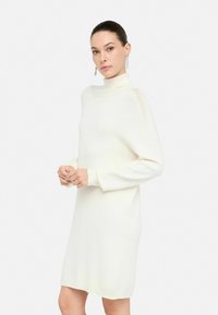 Abito bianco lavorato a maglia con un collo alto e maniche lunghe, caratterizzato da una vestibilità ampia e polsini a coste. Texture sottile e lunghezza fino a metà coscia.