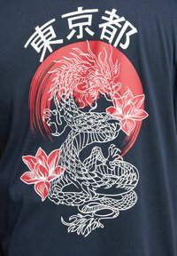 Dragon blanc avec des fleurs enroulé à l'intérieur d'un cercle rouge, caractères japonais au-dessus sur tissu sombre.