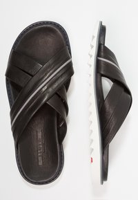 I sandali neri in pelle presentano cinghie incrociate con un accento grigio, una soletta testurizzata e una suola bianca seghettata.