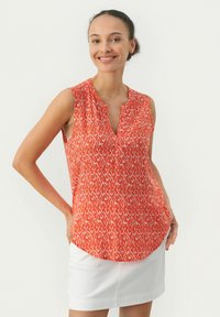 Ärmelloses Oberteil in leuchtendem Orange mit einem weißen abstrakten Muster, das einen geriffelten Ausschnitt und einen geschwungenen Saum aufweist. Hergestellt aus leichtem Stoff.