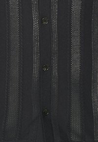 Černý kardigan s vertikálními pruhovanými pletenými panely, žebrovaným lemem a černými kulatými knoflíky po celé přední straně pro zapínání.