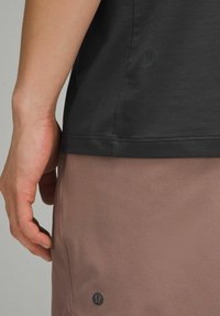 Schwarzes Kurzarmhemd mit glatter Textur, kombiniert mit hellrosa Sportshorts, die ein dezentes Logo-Detail am Saum aufweisen.