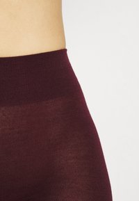 Leggings bordeaux a vita alta, in morbido e elastico tessuto a maglia con una superficie liscia, dotati di una fascia larga in vita per comfort e vestibilità.