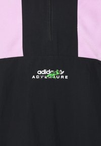 Musta ja vaaleanpunainen neljännesvetoketjullinen takki, jossa on valkoinen "adidas ADVENTURE" -logo, ja logon alla vihreä yksityiskohta. Tasainen pinta, urheilullinen muotoilu.