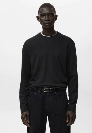 Czarna koszula z długim rękawem i okrągłym dekoltem, wykonana z gładkiego materiału. Noszona z ciemnymi dżinsami i czarnym paskiem, ozdobiona subtelnymi detalami przeszyć.