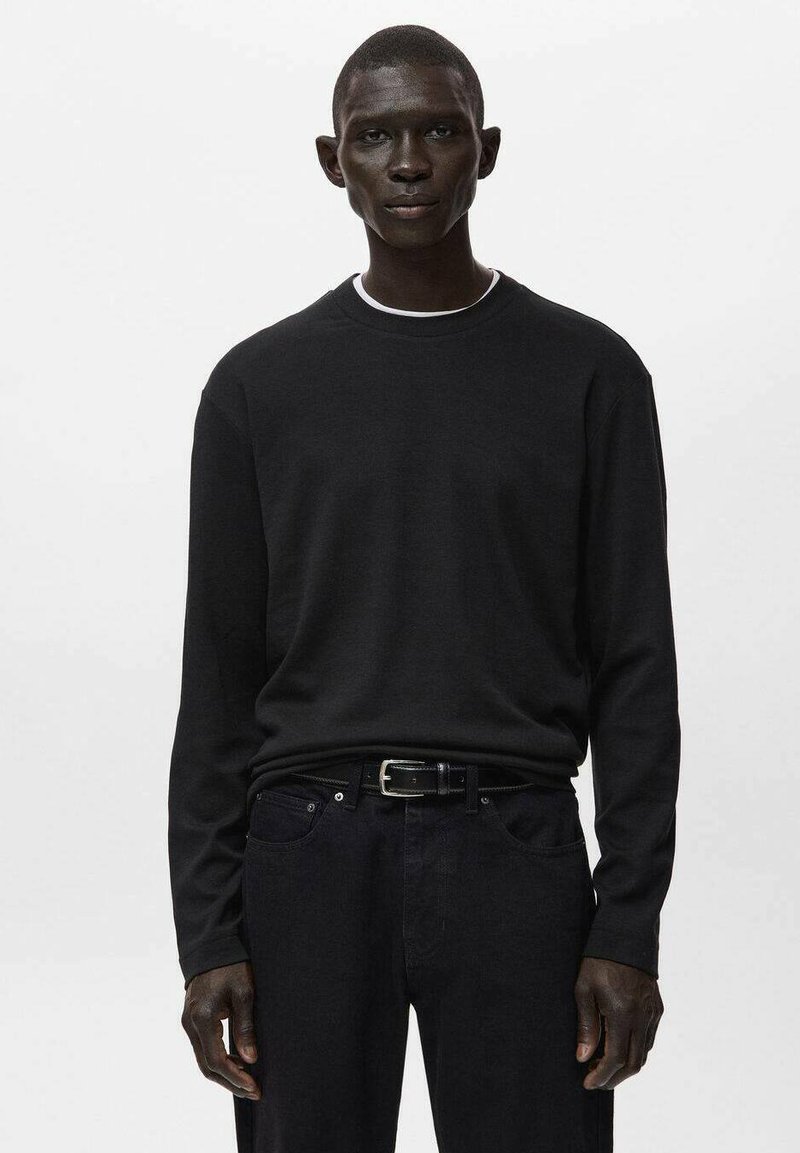 Musta pitkähihainen paita, jossa on pyöreä pääntie ja sileä kangas. Yhdistetty tummiin farkkuihin ja mustaan vyöhön, joissa on hienovaraiset saumaustiedot.