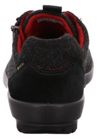 Schwarzer Wollmischschuh mit einer weichen, strukturierten Oberfläche, rotem Futter, schwarzer Gummisohle und kontrastierenden roten Nähten.