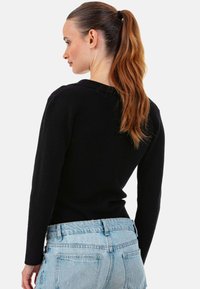 Pull noir en maille avec manches longues, encolure ronde et coupe ajustée, associé à un jean en denim bleu clair avec détails des poches arrière.