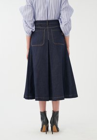 Denim midi krilo s širokim krojem, temno modre barve, vidno šivanje in zadnjimi žepi, v kombinaciji s črnimi čevlji z visoko peto.