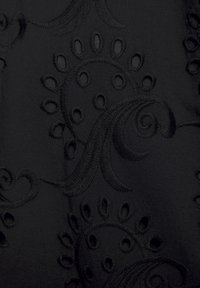 Schwarzer Stoff mit aufwendigen gestickten Mustern, die Schwünge und kreisförmige Ausschnitte zeigen. Sanfte Textur, markante Designelemente überall.